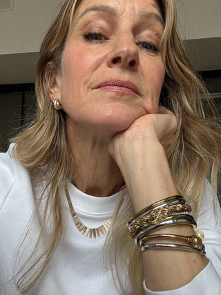 Woman wearing layered gold bracelets, necklace, and hoop earrings, showcasing elegant jewelry.