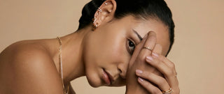 Woman wearing elegant gold rings, earrings, and necklace on neutral background